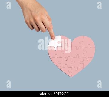 Adding the missing puzzle piece to heart-shaped jigsaw. Help, aid, donation concept Stock Photo