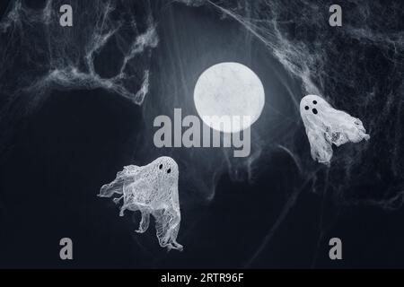 Ghosts of gauze on a dark background with glowing moon and spider web. Creative DIY Halloween decor. Halloween greeting card. Copy space. Stock Photo