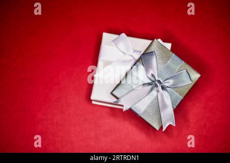 Silver Gift Box on top of a white gift box with bows isolated on red Stock Photo