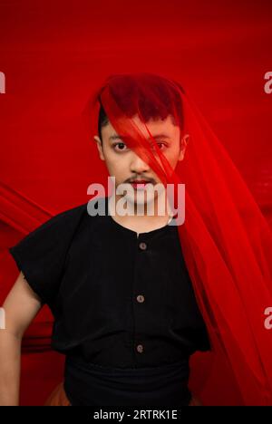 an Asian man standing in front of a red cloth with a red cloth hanging over his head during the day Stock Photo
