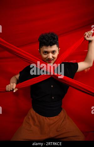 an Asian man stands in front of a red x-shaped cloth and holds it with both hands during the day Stock Photo