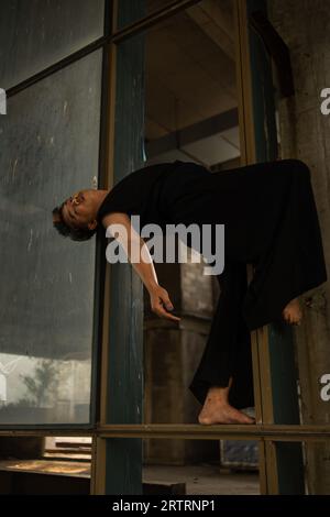 an Asian man hanging from the iron of an abandoned building while wearing a black shirt in the afternoon Stock Photo