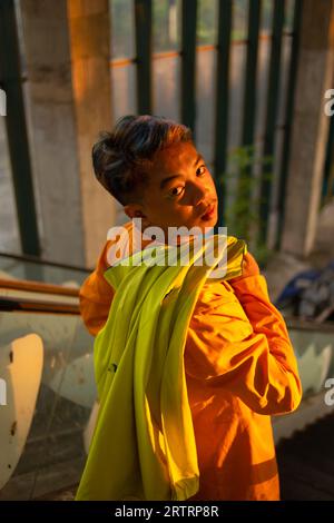 an Asian man standing in front of the window of an abandoned building while wearing a yellow blazer in the afternoon Stock Photo