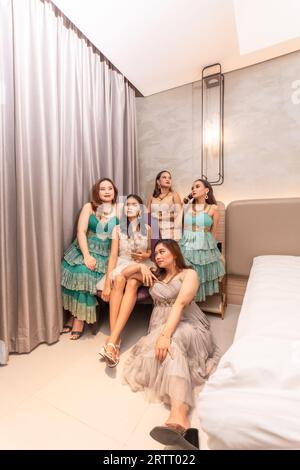 a group of Asian women in glamorous and luxurious clothes are sitting on the sofa with their friends after partying at night Stock Photo