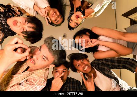 a group of Asian teenagers forming a circle and looking down with funny faces in an old room at night Stock Photo