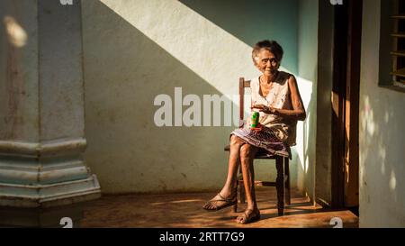 Baracoa, Cuba on January 7, 2016: In a Cuban house an old woman is enjoying a beer in the sun Stock Photo