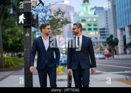 Business people discuss a project. Two young businessmen outdoors city looking cityscape. Businessmen communicating at meeting. Meeting of two Stock Photo