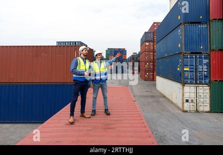 Shipment worker use a walkietalkie to point to container storage location, explain to colleague about planning for next shipment. Young worker with sa Stock Photo