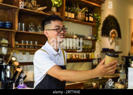 Vietnamese smiling waiter holding paper cups with coffee in a cafe Stock Photo