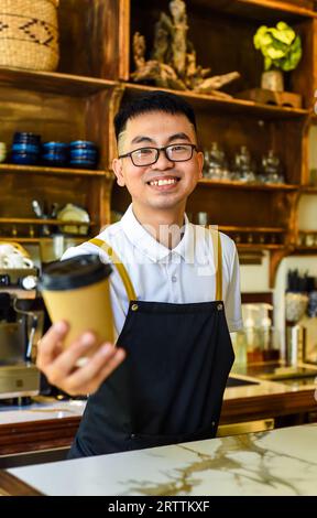 Vietnamese smiling waiter holding paper cups with coffee in a cafe Stock Photo