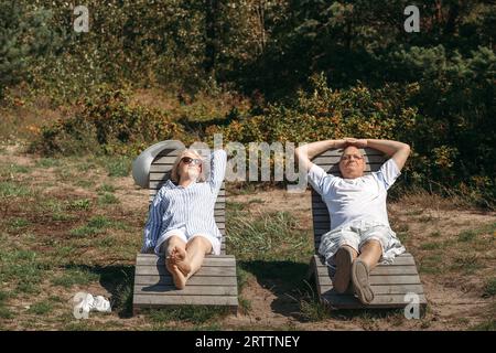 A couple of cute elderly people are lying on sunbeds, basking in the sun. Stock Photo