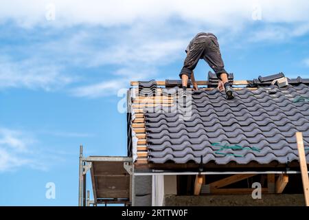 ceramic roof of a new building, worker installs tiles on wooden beams Stock Photo