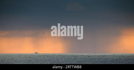 Rain on the distant horizon in the ocean. Dark clouds and rain poured in the evening. Stock Photo