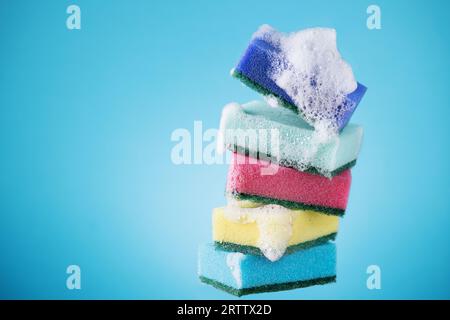 Stack of kitchen multi coloured sponges with detergent foam on blue background. Dish washing sponges. Stock Photo