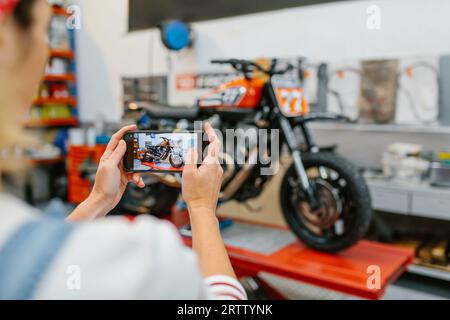Female mechanic taking photo to motorcycle repaired on garage Stock Photo