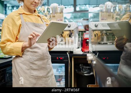 Manager of supermarket in apron working online on digital tablet Stock Photo