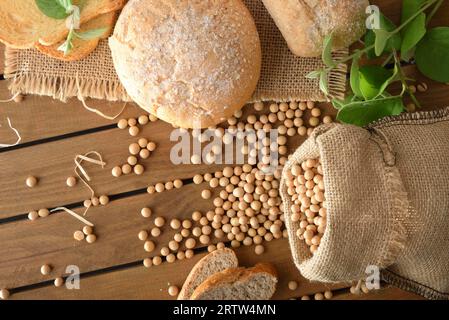 Sack full of soybeans on rustic wooden table with soybean bread and leaves in the countryside. Top view. Stock Photo