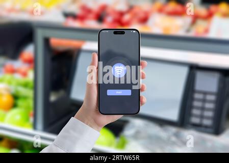 Woman holds a smartphone, displaying an NFC payment. Grocery store market in background. Concept of faster and more efficient shopping with apps Stock Photo