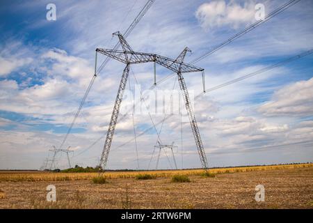 Power transmission tower in Ukraine in summer. Overhead wires of high-voltage power transmission line supports through a field with corn in summer Stock Photo