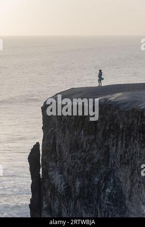 Pregnant woman standing near a cliff on the beach at sunset Stock Photo