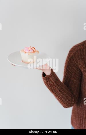 A woman in a red sweater holding a plate with a pink sprinkled c Stock Photo
