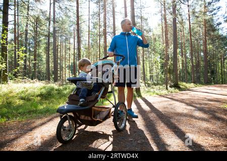 Athletic man in sportswear running with baby stroller at sunny morning in city park during fatherhood time. Stock Photo