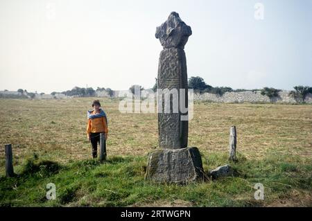 Woman standing in field by Penmon Cross c 1000 AD, Penmon Priory, Anglesey, North wales, UK 1966 Stock Photo