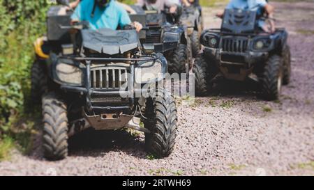 Group of riders riding ATV vehicle crossing forest rural road, process of driving a rental vehicle, all terrain quad bike vehicle, during off-road tou Stock Photo