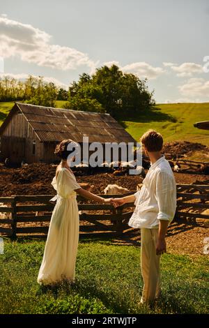 rustic wedding in boho style, back view of newlyweds holding  hands and looking at livestock in farm Stock Photo