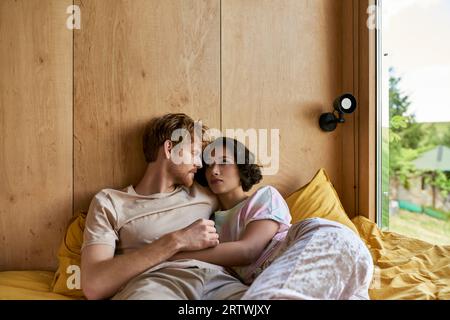 interracial couple having tender moment while lying together on bed and looking at each other Stock Photo