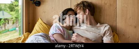 interracial couple having tender moment, lying together on bed and looking at each other, banner Stock Photo