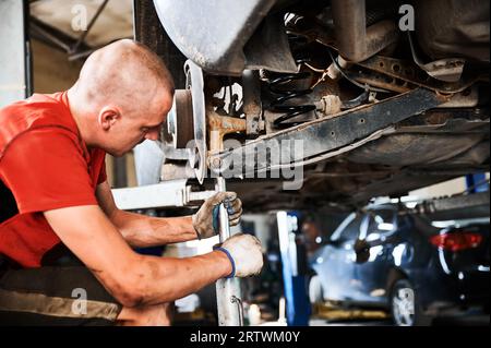Professional worker, repairman changing car wheel, fixing problem. Hardworking, strong man working in auto, servicing center. Concept of repairing, maintaining car. Stock Photo
