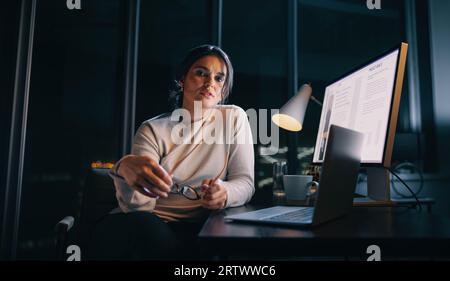 Determined businesswoman balances work and home life, putting in late hours at her home office. Woman working with her laptop and computer, planning a Stock Photo