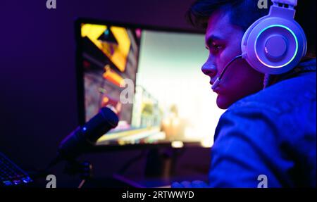 Video game player getting into the gaming world as he settles into his computer setup, with a microphone in front of him. Man delivering a gameplay br Stock Photo
