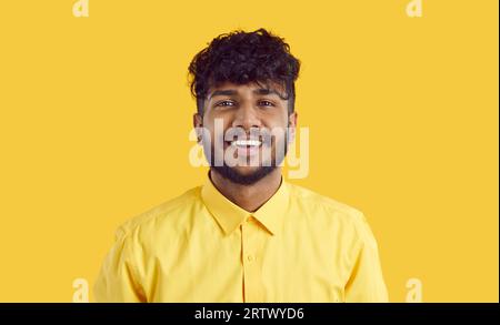 Young happy ethnic Indian man millennial with beard and curly hair stands on yellow background Stock Photo