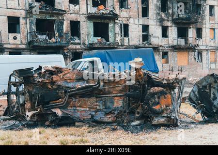 A burned-out car next to a residential building destroyed by rocket fire. War in Ukraine. Terror of the civilian population Stock Photo