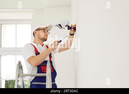 Male technician installs CCTV camera on wall in new bright office of business center. Stock Photo