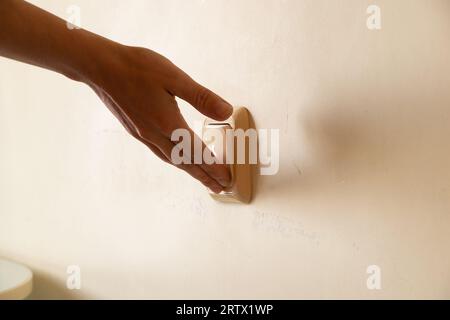 A woman's hand turns on the light on the wall in the apartment, the switch on the wall, turn it on and off Stock Photo