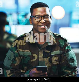 Portrait, phone and a military black man in a control room for surveillance, communication or networking. Face, smile and a confident young army Stock Photo
