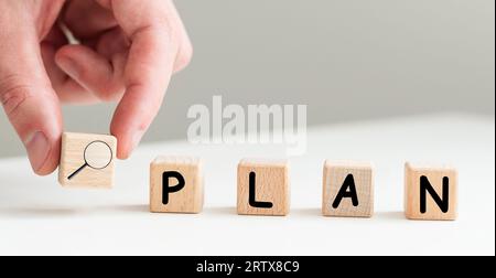 Businesswoman hand holding wooden cube with PLAN text on table background. Goals, success, strategy, solution and business concepts Stock Photo