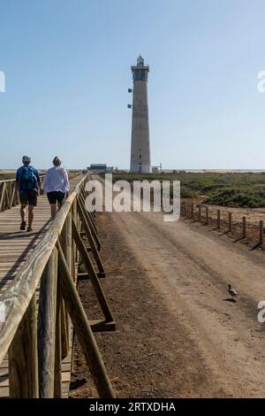 A couple walks hand in hand towards the beach where the lighthouse is located, Matorral, Fuerteventura, Canary Islands, Spain Stock Photo