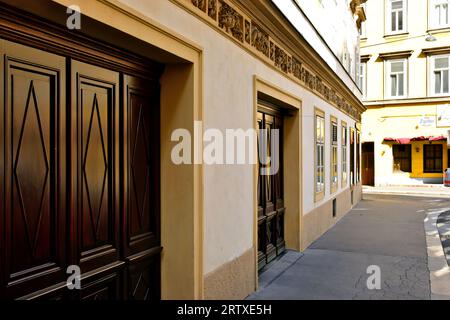 diminishing street perspective. residential building. stained brown carved wood gates and ornate stucco trim. cracked grey asphalt sidewalk pavement Stock Photo