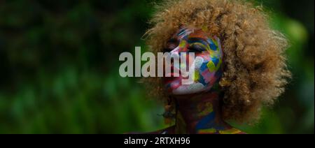 Nueva Loja, Sucumbios / Ecuador - September 3 2020: Portrait of young black woman with colorful painted face with closed eyes with relaxed expression Stock Photo
