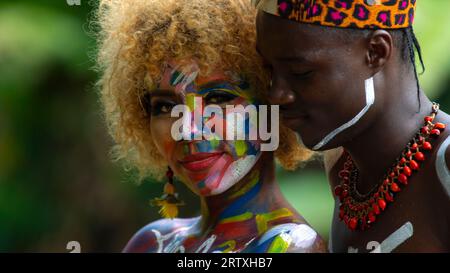 Nueva Loja, Sucumbios / Ecuador - September 3 2020: Portrait of black couple in love with color painted body hugging in a forest with unfocused green Stock Photo