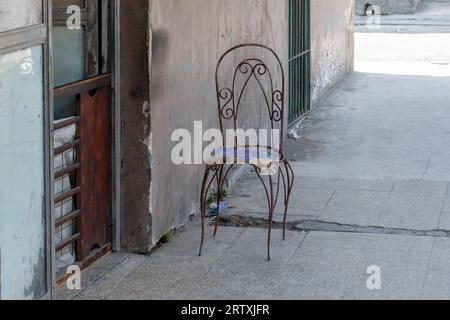 Havana, Cuba, 2023, An old rusty metal chair on a broken sidewalk. Weathered wall and door of a house. Stock Photo