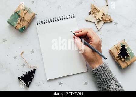 Female hand writing in a empty notebook. Festive decoration on table. Flat lay. New Year's plans and goals. Stock Photo