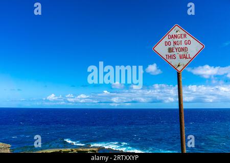 Danger warning sign keep visitors at bay at Lanai Lookout on the Kalanianaole Highway in Oahu, Hawaii. Strong waves and Pacific Ocean current at edge Stock Photo