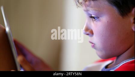 Digital native child addicted to tablet device. Young boy absorbed by screen playing video-game in competition Stock Photo