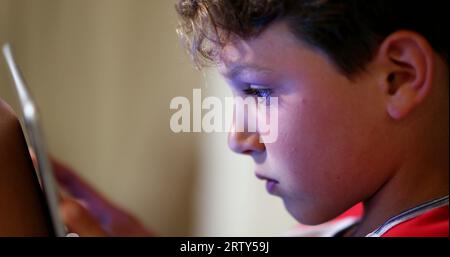 Digital native child addicted to tablet device. Young boy absorbed by screen playing video-game in competition Stock Photo