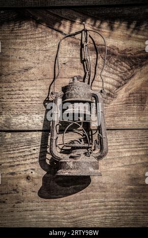 Rusty old broken oil lamp hang on wooden shack wall Stock Photo